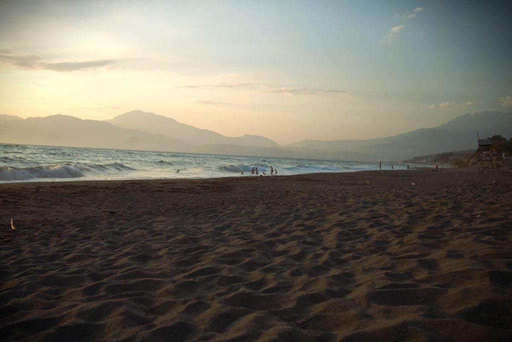Kommos Beach, Creta del sud, al tramonto. Sabbia scura, onde e profili di montagne.