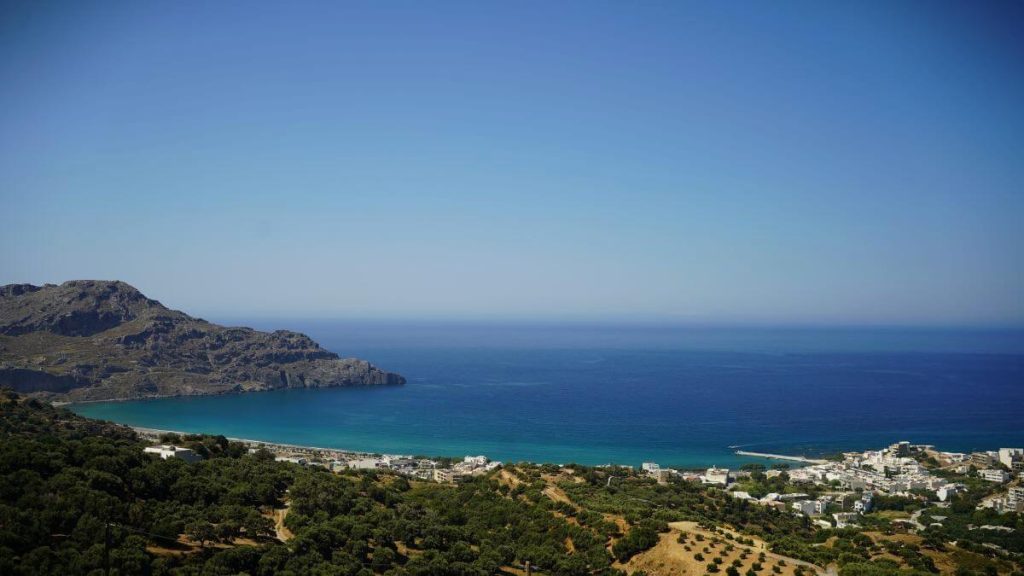 Panorama da Myrthios, Creta. Mare turchese, cielo sereno e montagne intorno.